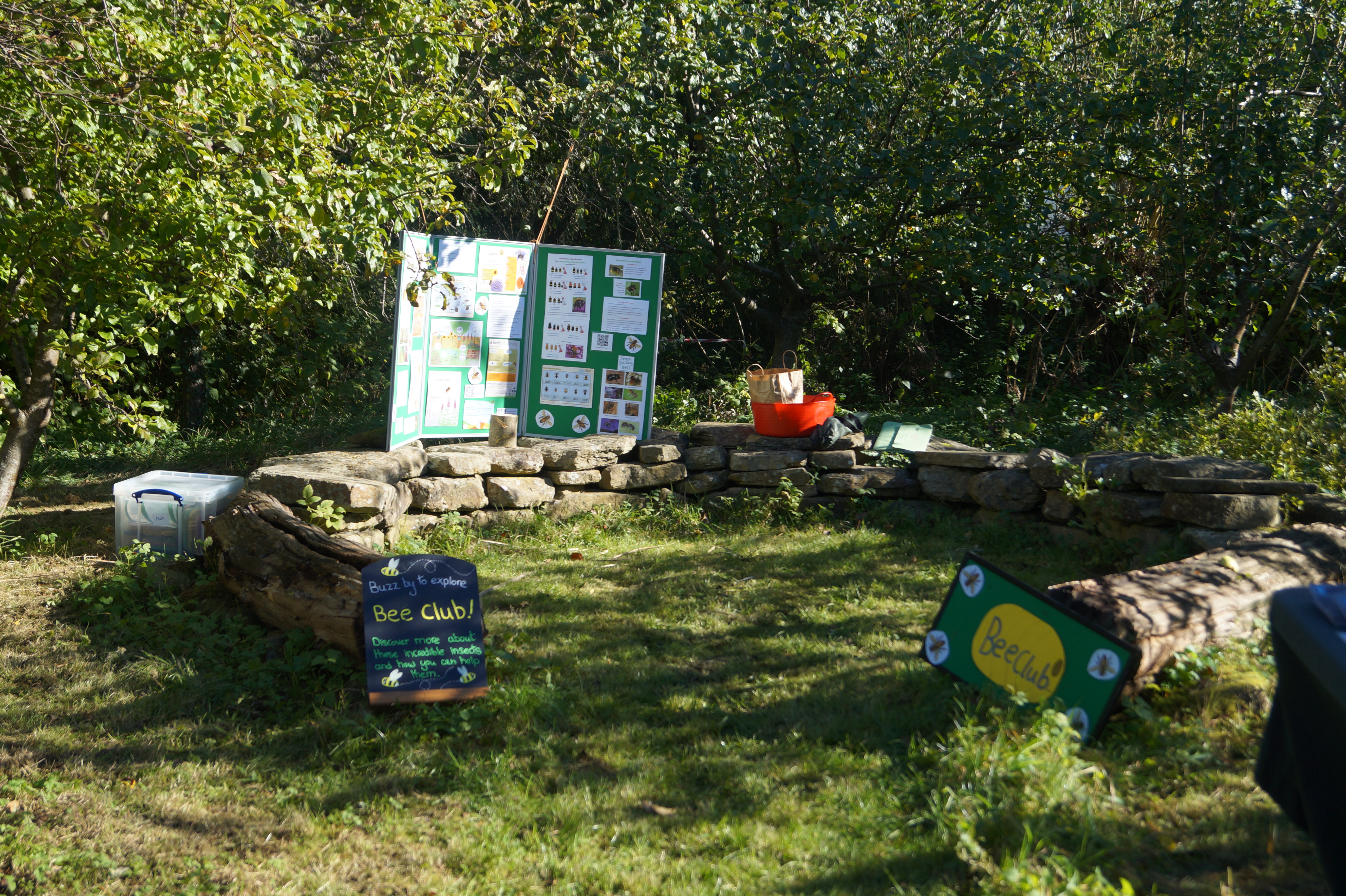 Stone bench surrounded by trees with info board and signs for Bee Club